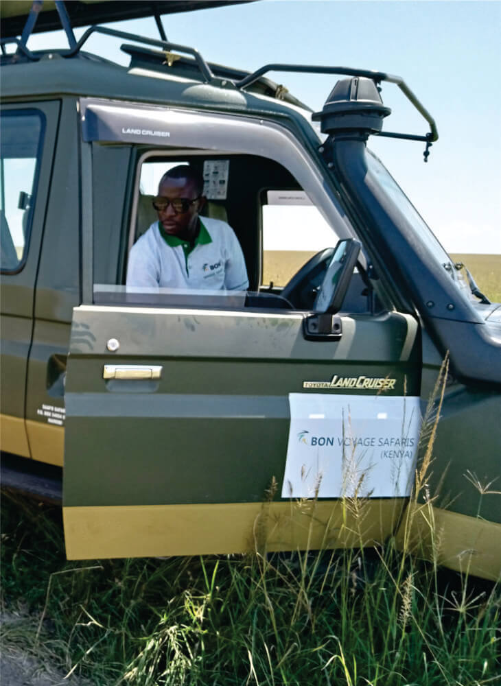 a driver guide putting on shirt with Bon Voyage Budget Safari in Kenya logo getting out of a green 4x4 jeep in Masai Mara on jeep tour