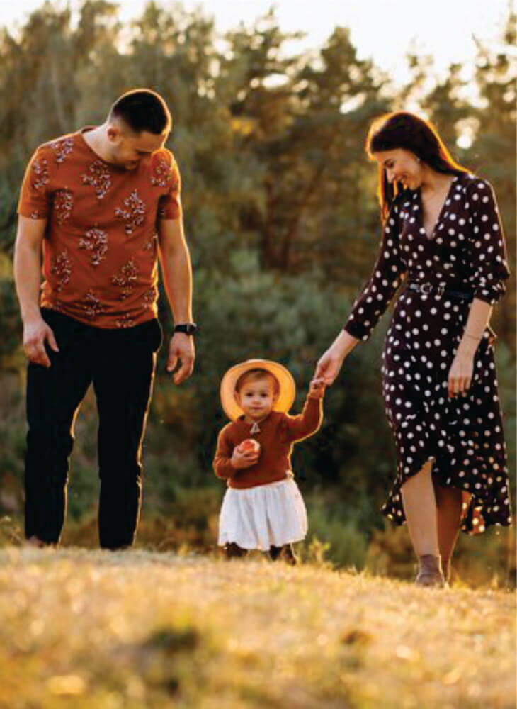 father, mother and child walking in field  near trees in Amboseli on family safari in Kenya