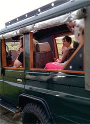 green jeep carrying group of travelers and guide on dirt road in Masai Mara on jeep joining safari tour