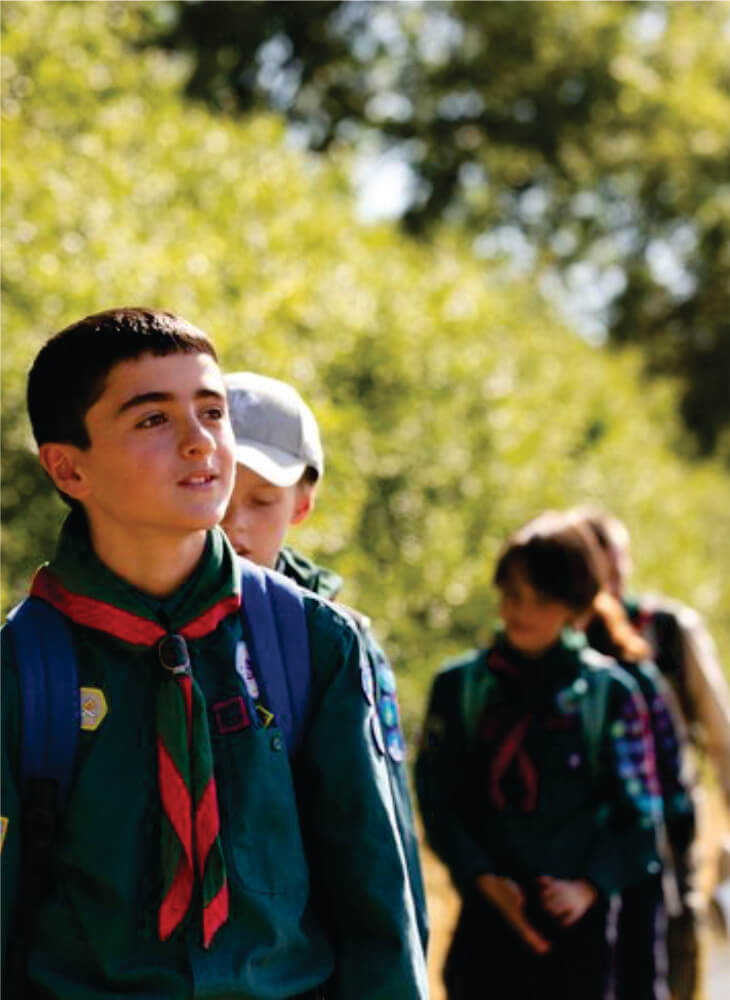 Kids in green scouts uniforms carrying backpacks and walking near trees in Masai Mara on Kenya and Tanzania safari with kids