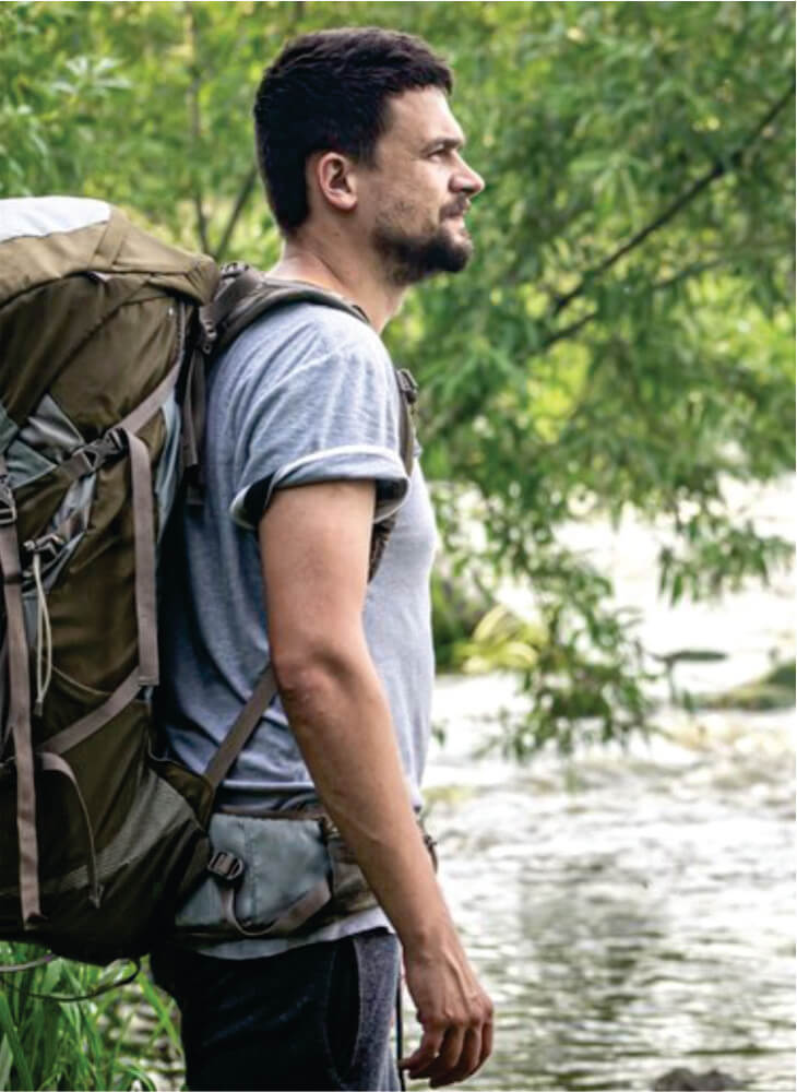 male budget traveler with a large backpack stands near Mara river on affordable Masai Mara camping safaris in Kenya