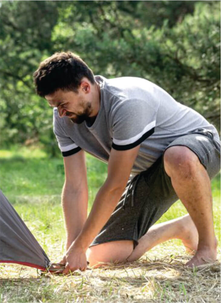 Man setting up his tent for camping near trees in Masai Mara on affordable Masai Mara camping safaris in Kenya