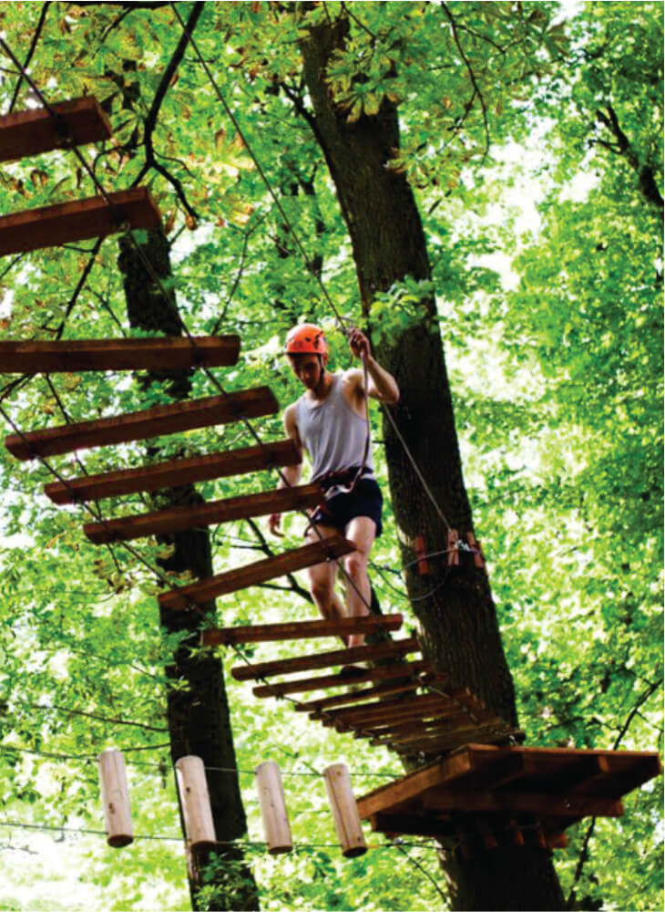 Man steps on the long wooden boards hanging in the air in an adventure park in Kenya on adventure camping safaris