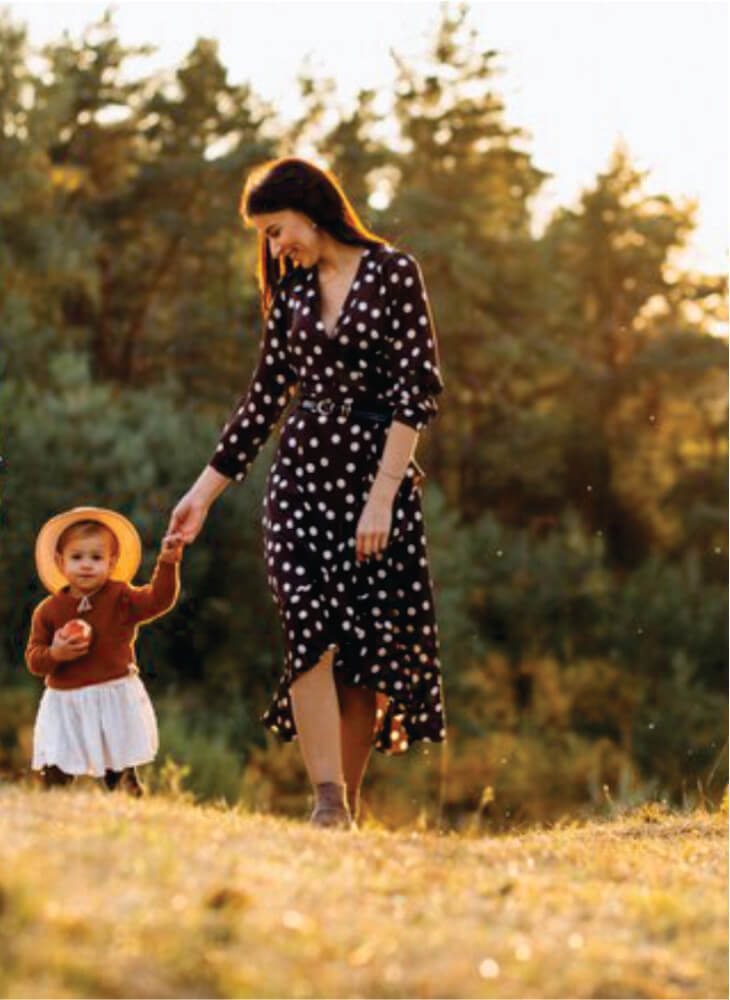 mother in black and white dress with child walking in field near trees in Amboseli on family safari in Kenya