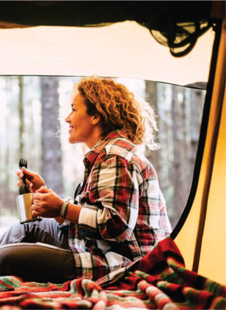 woman sitting down inside a yellow tent looking at the panorama outside and holding silver cup on Kenya budget camping safari in Amboseli