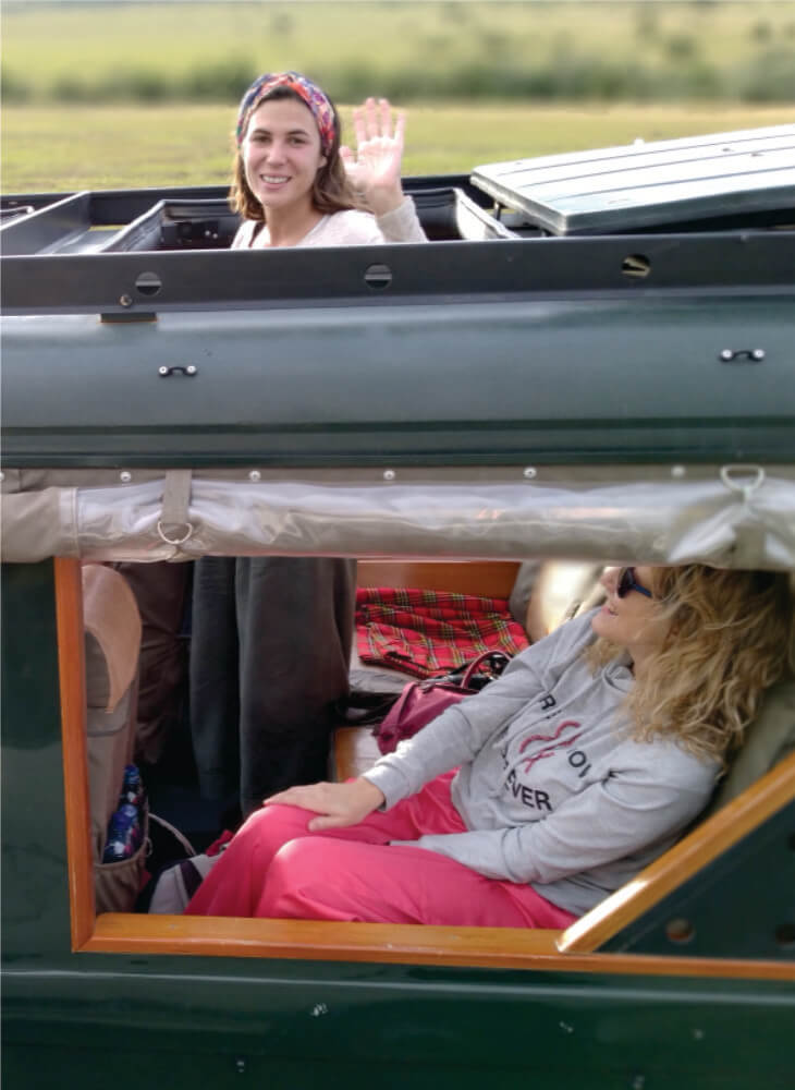 young lady sitting and woman waving from the pop-up roof of a green jeep on 10 days Masai Mara camping safaris in Kenya