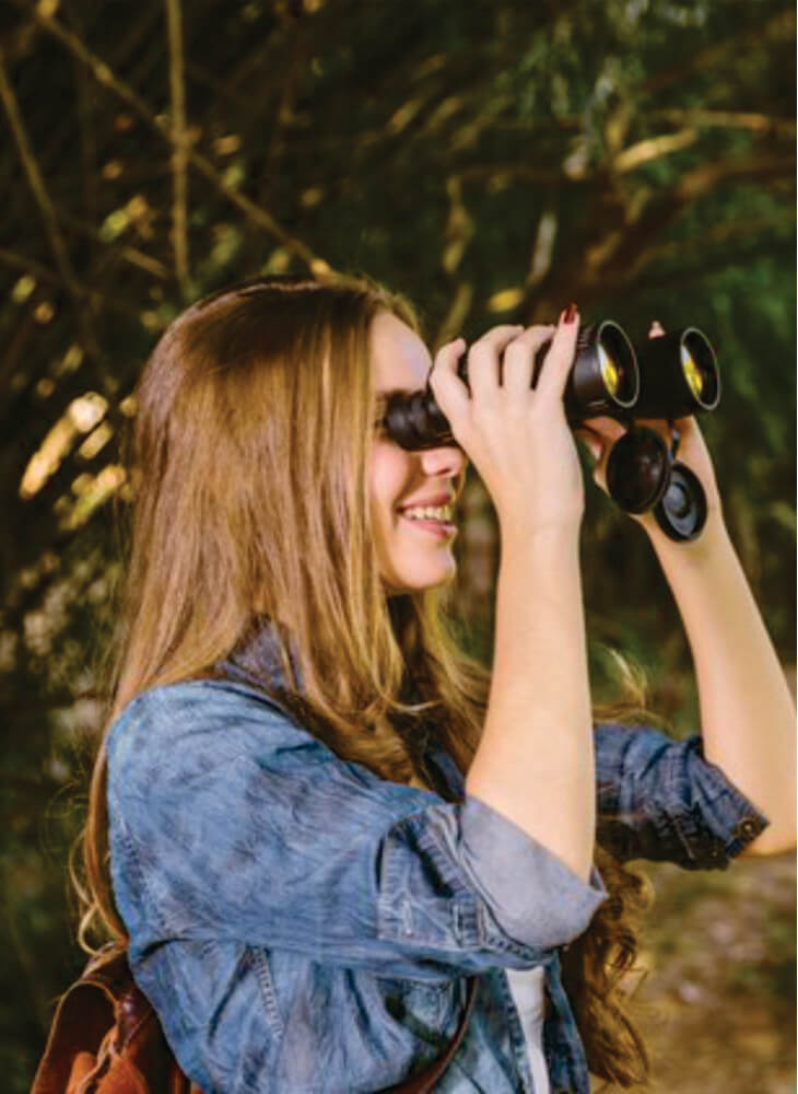 young woman with brown backpack smiling and looking through binoculars in Masai Mara on safari to Serengeti and Masai Mara