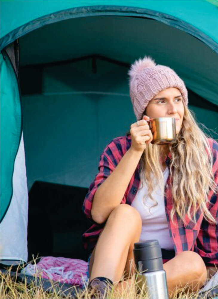 blonde woman in hat relaxing and drinking tea and looking away, sitting in green tent in Masai Mara on Kenya camping safari tour
