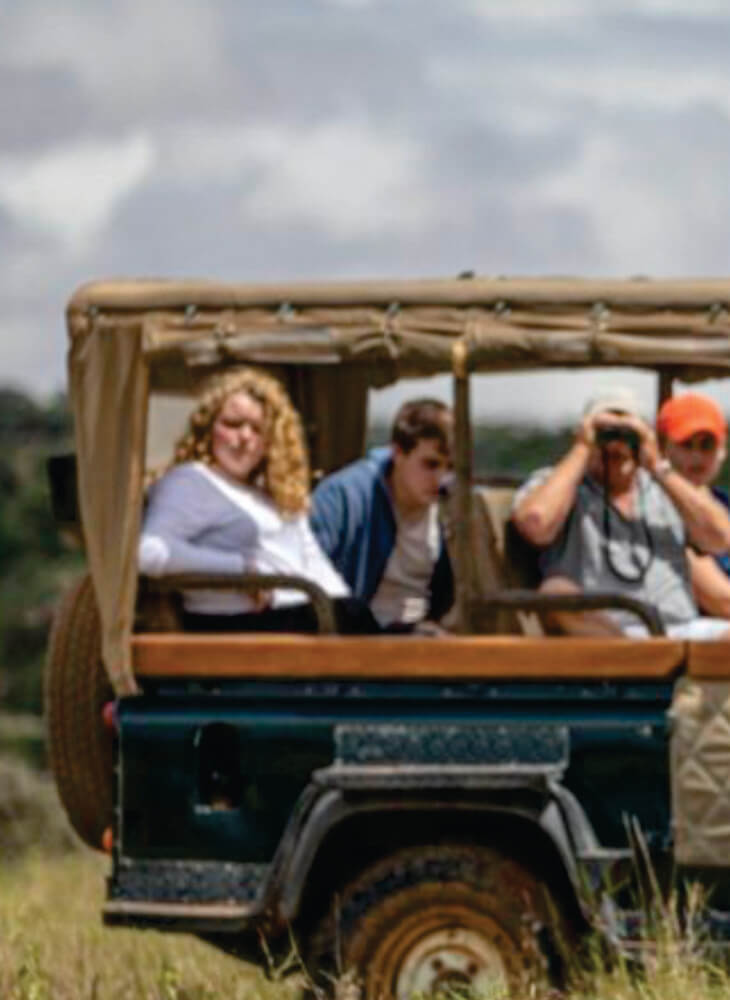 four tourists taking photographs and enjoying the ride in a green 4x4 jeep in Masai Mara on group joining budget safari jeep tours
