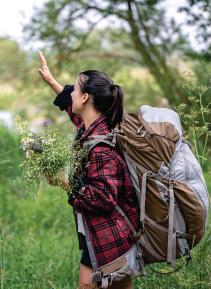 girl with a large travel backpack and a bouquet of wildflowers near trees on affordable 5-day Masai Mara and Lake Nakuru safari