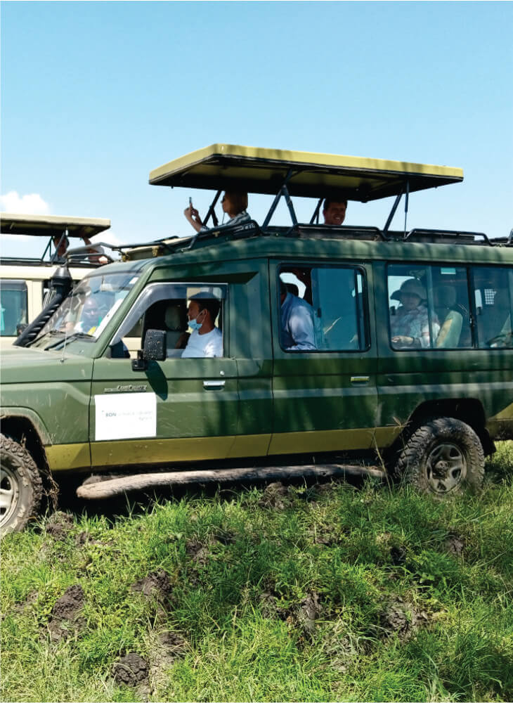green 4x4 jeep with pop up top carrying group of tourists on green grass field in Masai Mara during Masai Mara joining jeep safari tours
