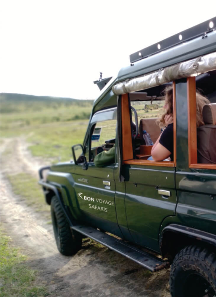 green luxury 4x4 jeep carrying tourist and guide on dirt road in Masai Mara on affordable luxury safari in Kenya