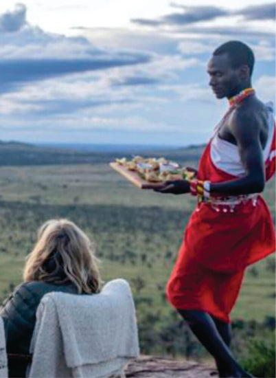 Maasai man in traditional red shuka serving food to woman on field in Masai Mara on luxury Mara Serena Safari Lodge Masai Mara group tour