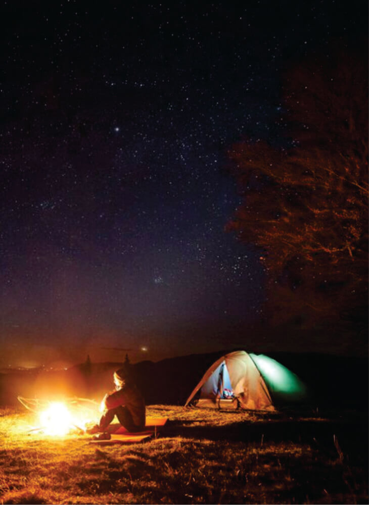 man sitting near bright burning bonfire and illuminated tourist tent at nighttime, enjoying camping night on Masai Mara budget camping safaris in Kenya