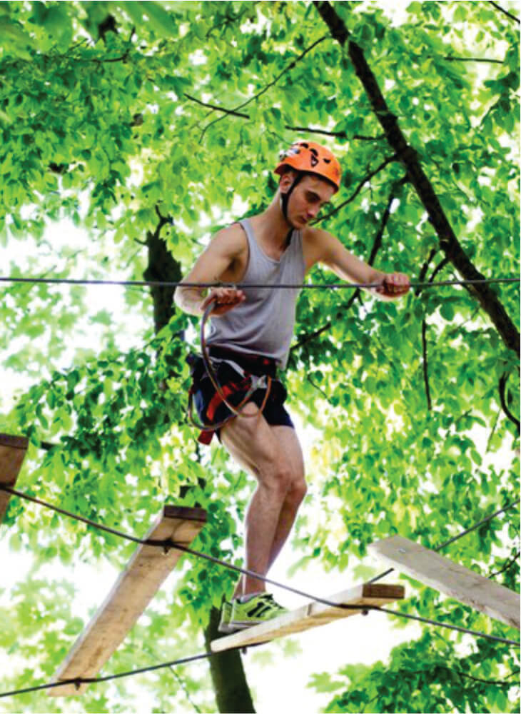 Man steps on the wooden boards hanging in the air in an adventure park in Kenya on Kenya adventure safari tour