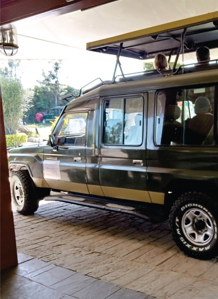 side view of custom-built 4x4 green jeep with pop-up-top roof parked near hotel in Amboseli on private jeep safari tour in Kenya