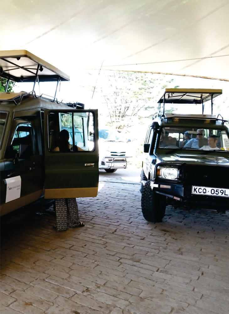 group of tourists boarding two green jeeps with pop-up-top roof parked in front of hotel in Masai Mara on private Africa jeep safari tours