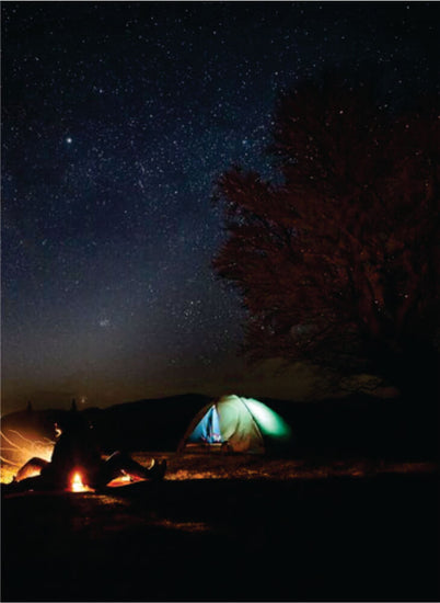 two travelers sitting near bonfire and  green budget backpacking tent at nighttime in Masai Mara during Kenya camping safari tour