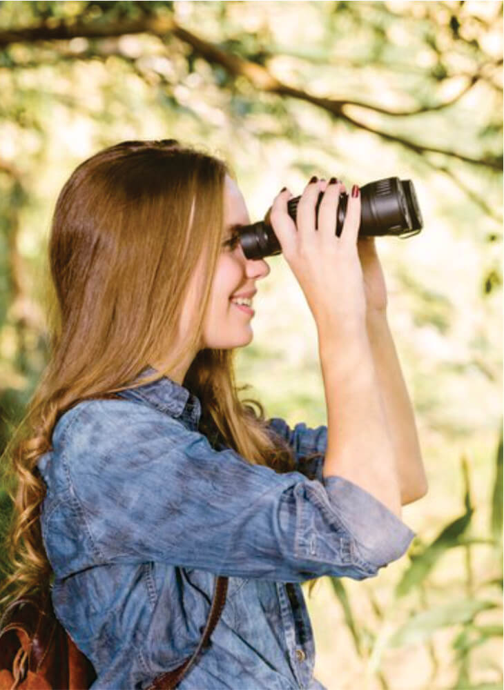 young woman in blue blouse with brown backpack looking through binoculars on safari to Serengeti and Masai Mara